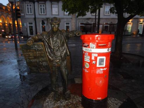 A bronze statue of a man is delivering post into a red post box