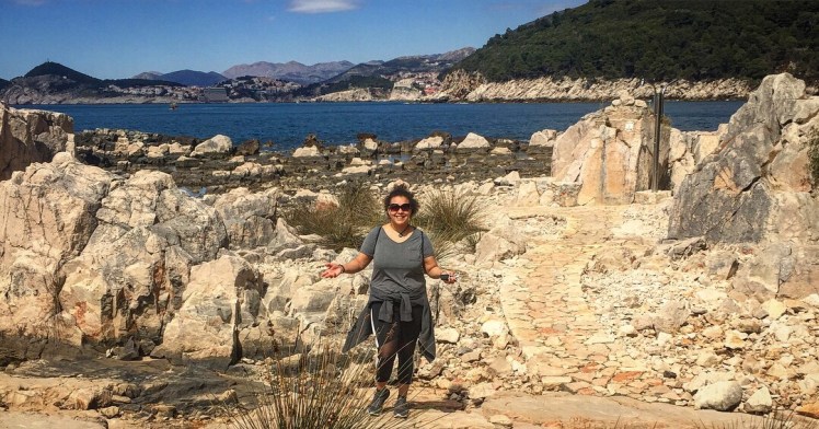 Jemma Reid standing in the middle of the rocks of Lokrum Island in Croatia. You can see the sea in the background with more islands behind that where Croatia lie.