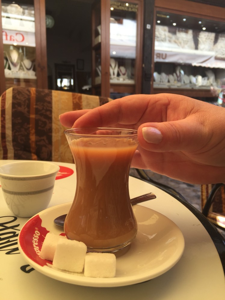 Turkish tea in a small vase like glass with three chunks of uneaten sugar next to it. A womans hand is about to grab the drink.