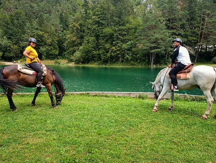 Stopping for some grass to eat whilst on horseback. There is a brown horse called Charlie and a white horse called Tim.