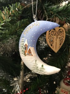 Half moon Christmas tree decoration is blue and fades into white. Has a small cabin drawn on with “Prague” written at the top. 