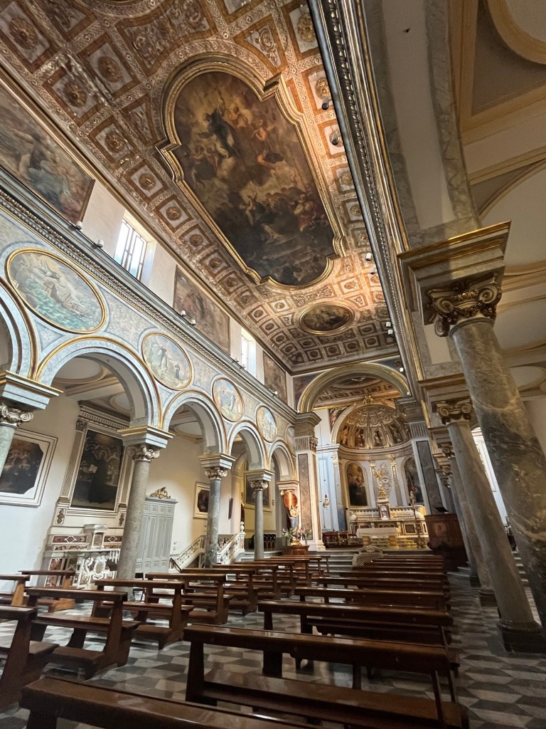 A church with tall ceilings. All painted with imagery. Pews that are wooden and brown are down the bottom on the floor. 